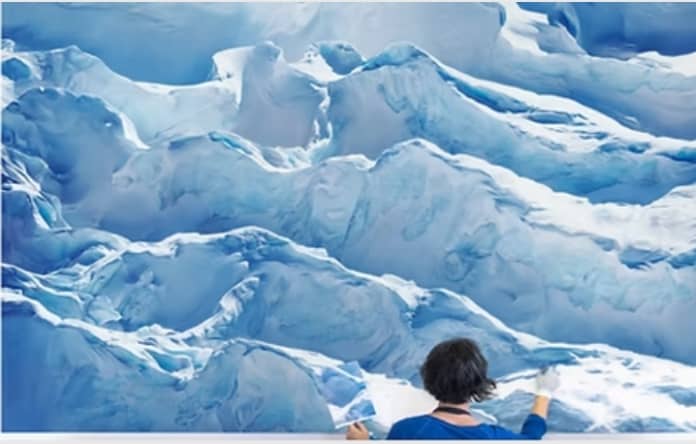 Large-scale glacier painting in progress by a pastel artist on a blue-toned ice landscape.
