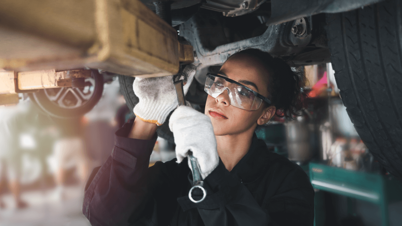 A woman in safety glasses works on a car, despicting the blog article how to make an auto repair website effectively.