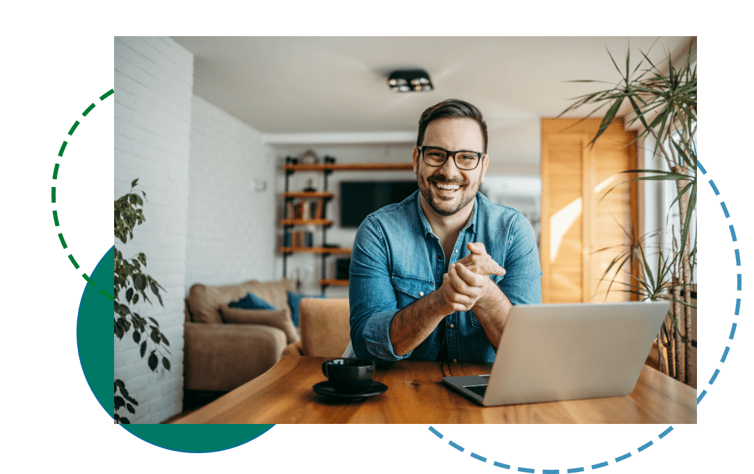 Smiling man sitting at a dining table with a laptop and coffee mug in front of him