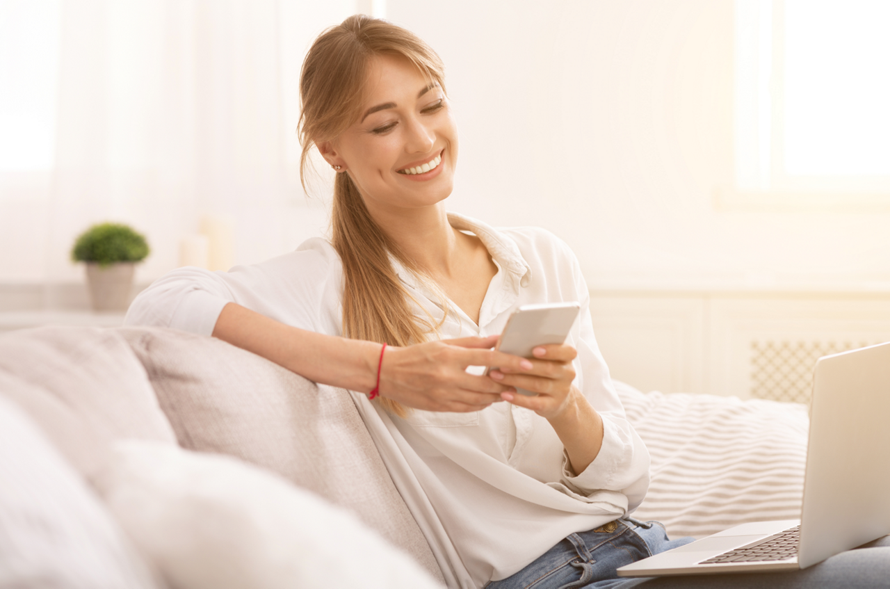 Young woman sitting on a white couch with a laptop on her lap.